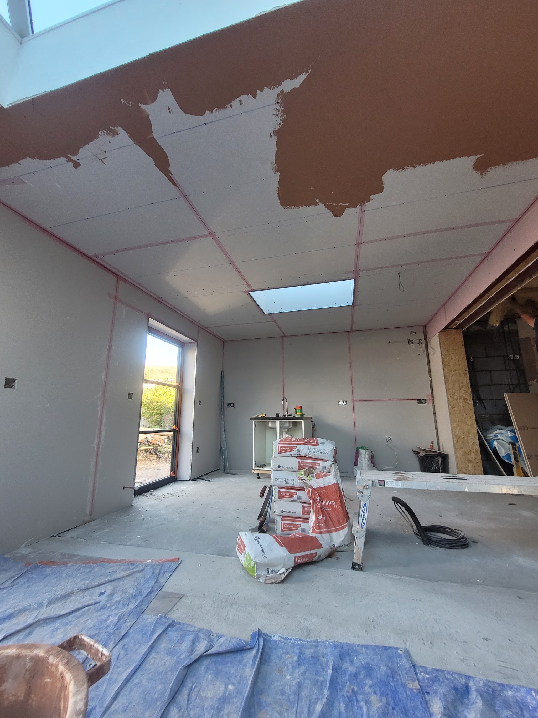 Extension ceiling part way through skimming, with the floor covered in protective sheets