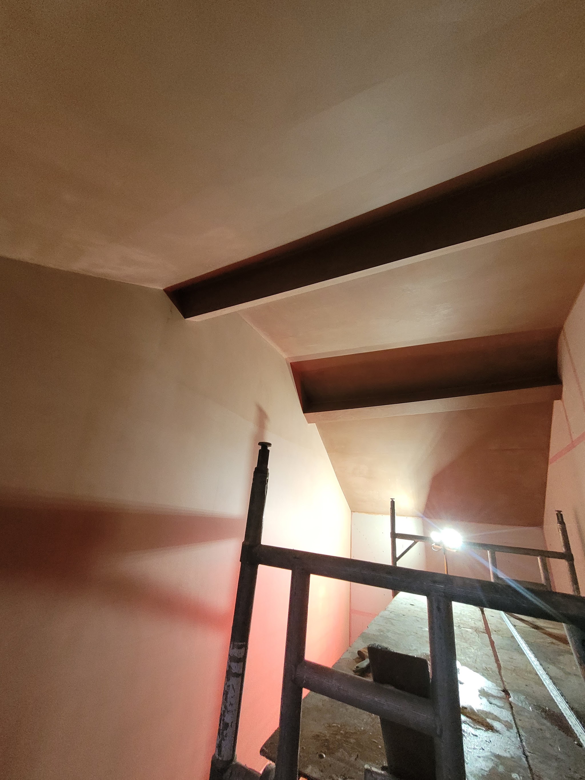 Fresh skim on the walls and sloping ceiling around a beam, with a scaffold tower in place