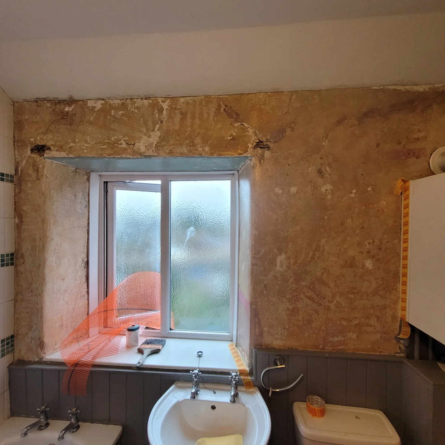 Bathroom walls of bare old plaster around the window, before skimming